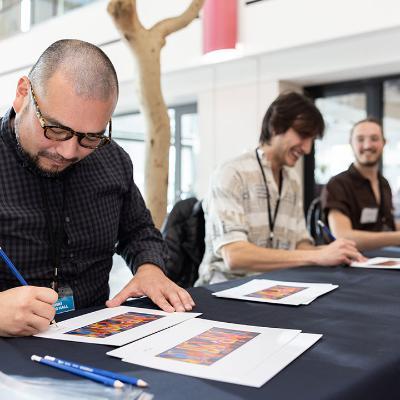 Three people at the LMU Arthur P. Carroll Jr. Wine Classic take pen to paper.