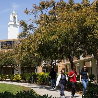 Three students walk on the LMU campus with a view of the bell tower of Sacred Heart Chapel behind them.
