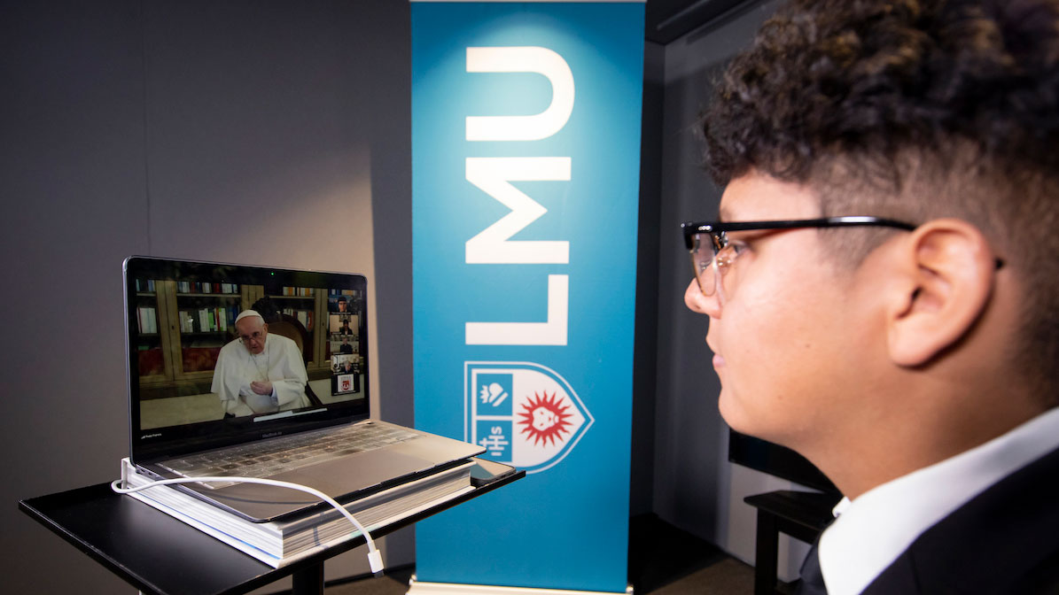 A student in front of a laptop with Pope Francis on the screen