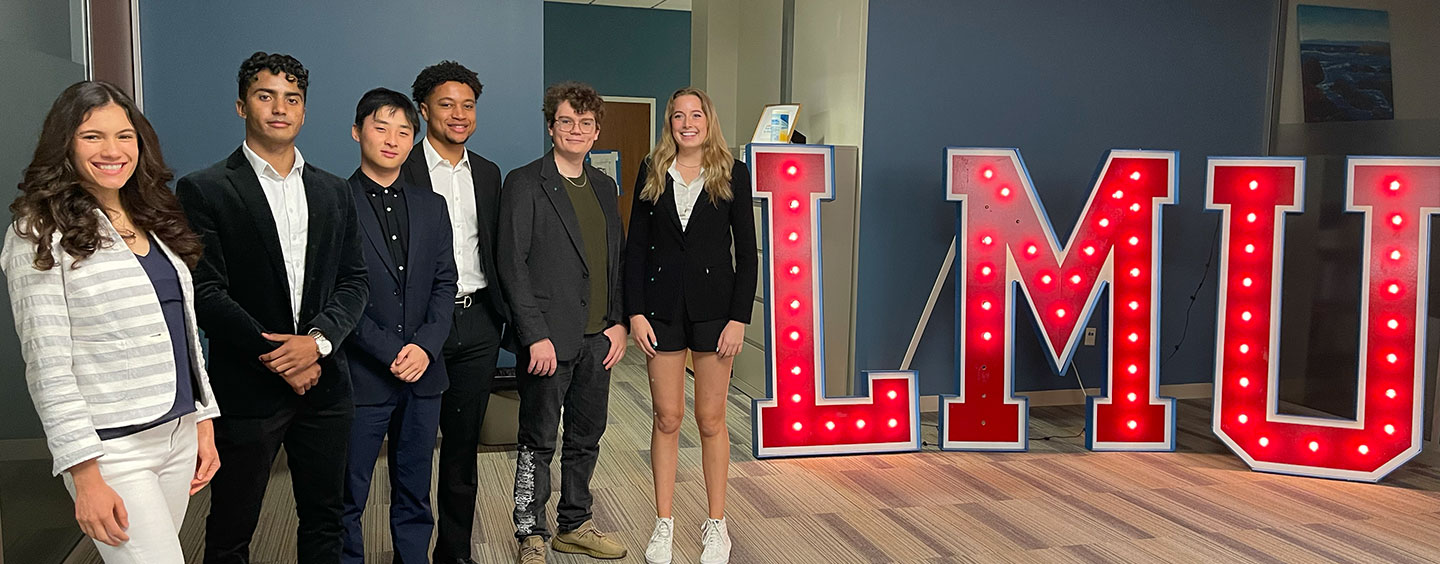 A group of students in professional attire with an illuminated LMU lettered sign behind them