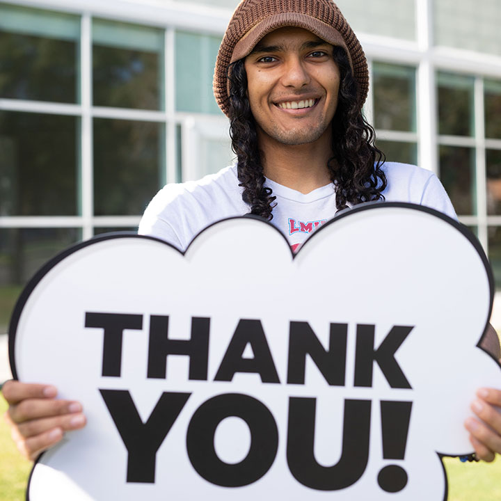 A student holding a sign saying Thank You in front of the Student Gallery