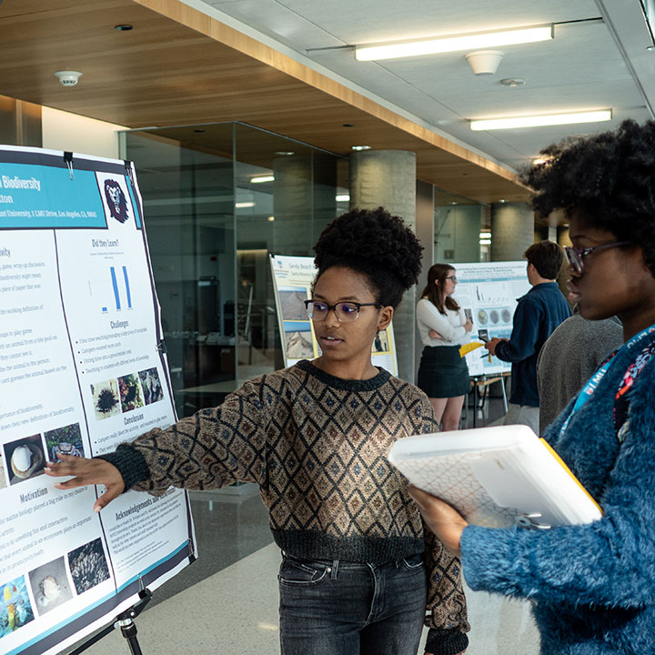 A student presenting a complex research project board at a large event