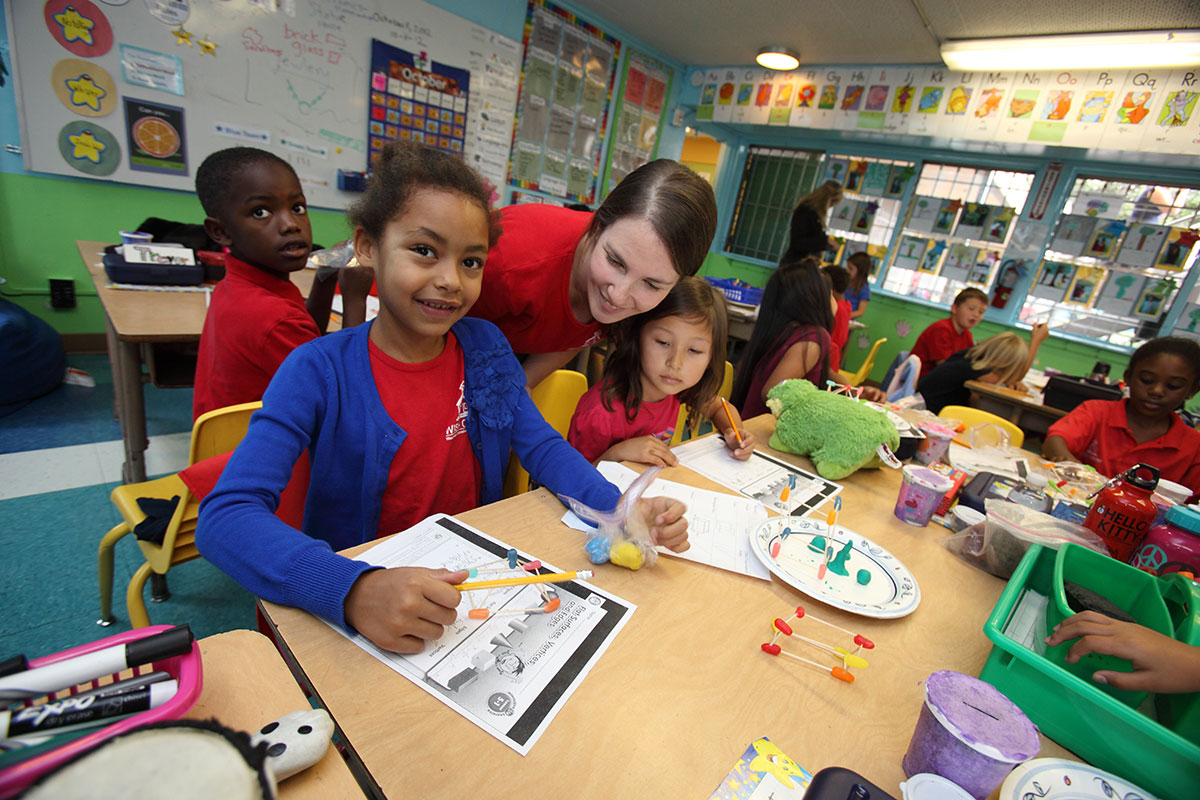 Elementary students doing arts and crafts with clay and pipe cleaners with the teaching observing and helping