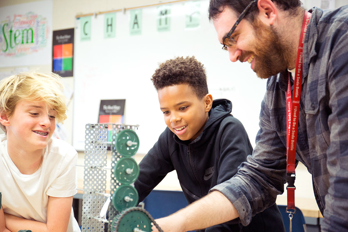 Two middle school students working with a teacher on an erector set model with interlocking gears