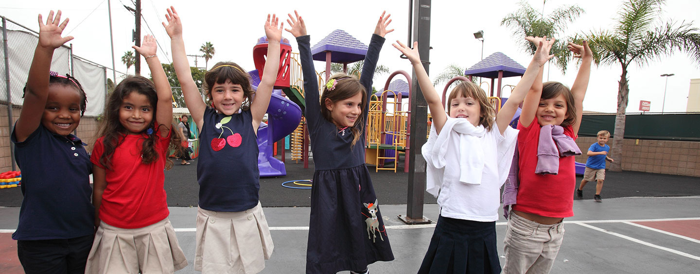 Elementary students raising their hands in the air in excitement at a playground