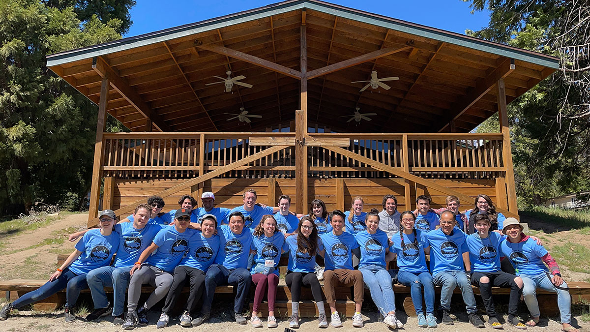 Students posing for a group portrait during Campus Ministrys Encounter Retreat in Lake Arrowhead in front of a large cabin