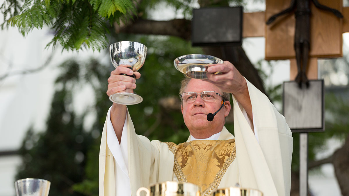 Edward Seibert, S.J., blesses the Eucharist at an outdoor Mass