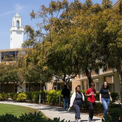 Three students walk on the LMU campus with a view of the bell tower of Sacred Heart Chapel behind them.