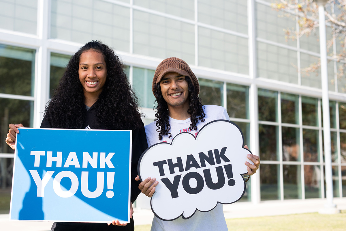 Two smiling LMU students hold up signs that say 