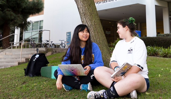 Two students sit in front of the Charles Von Der Ahe Building